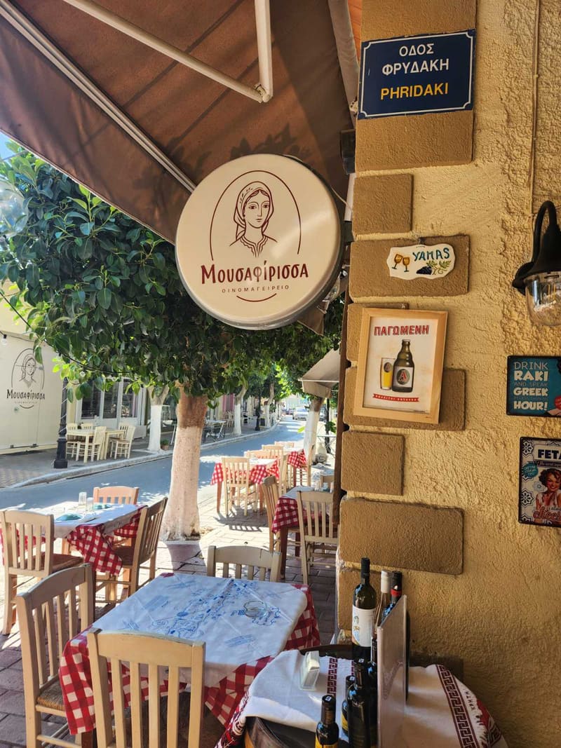 Η ταμπέλα της Μουσαφίρισσας και τα τραπέζια στον πεζόδρομο, γωνία Φρυδάκη, Καστέλλι Κισσάμου